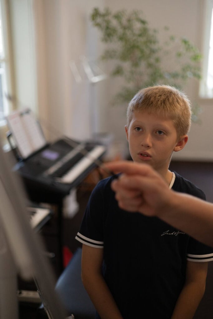 Junge im Unterrichtsraum der Musikwerkstatt, im Hintergrund Keyboards und Notenständer