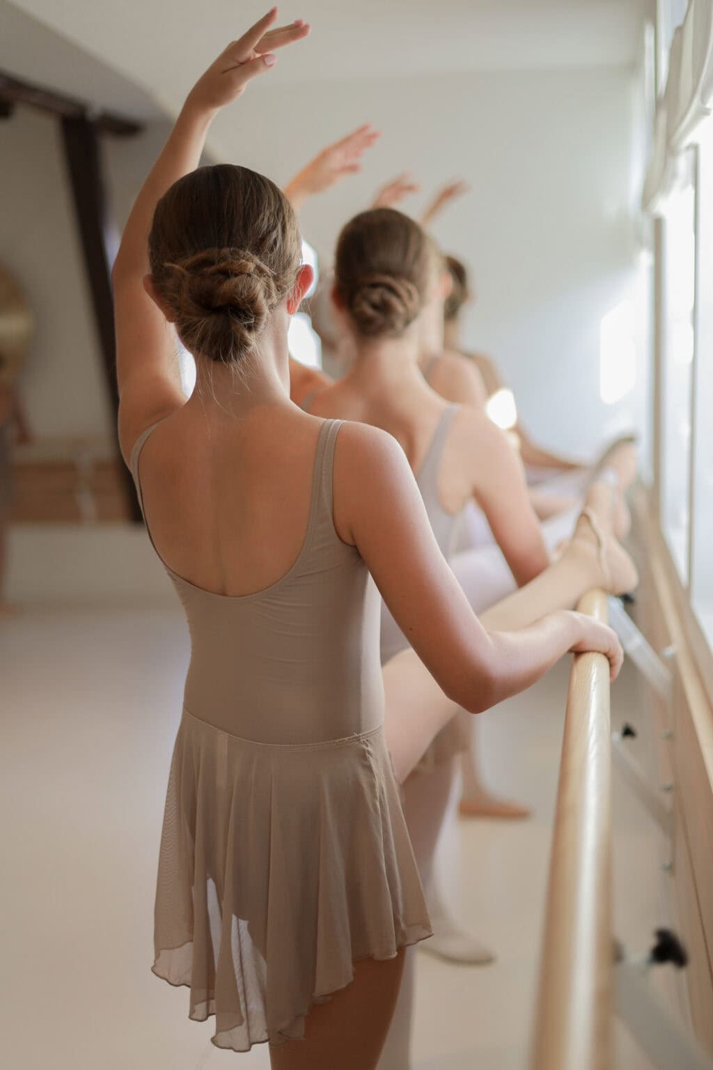 Ballettschülerin an der Stange, den Arm nach oben geöffnet