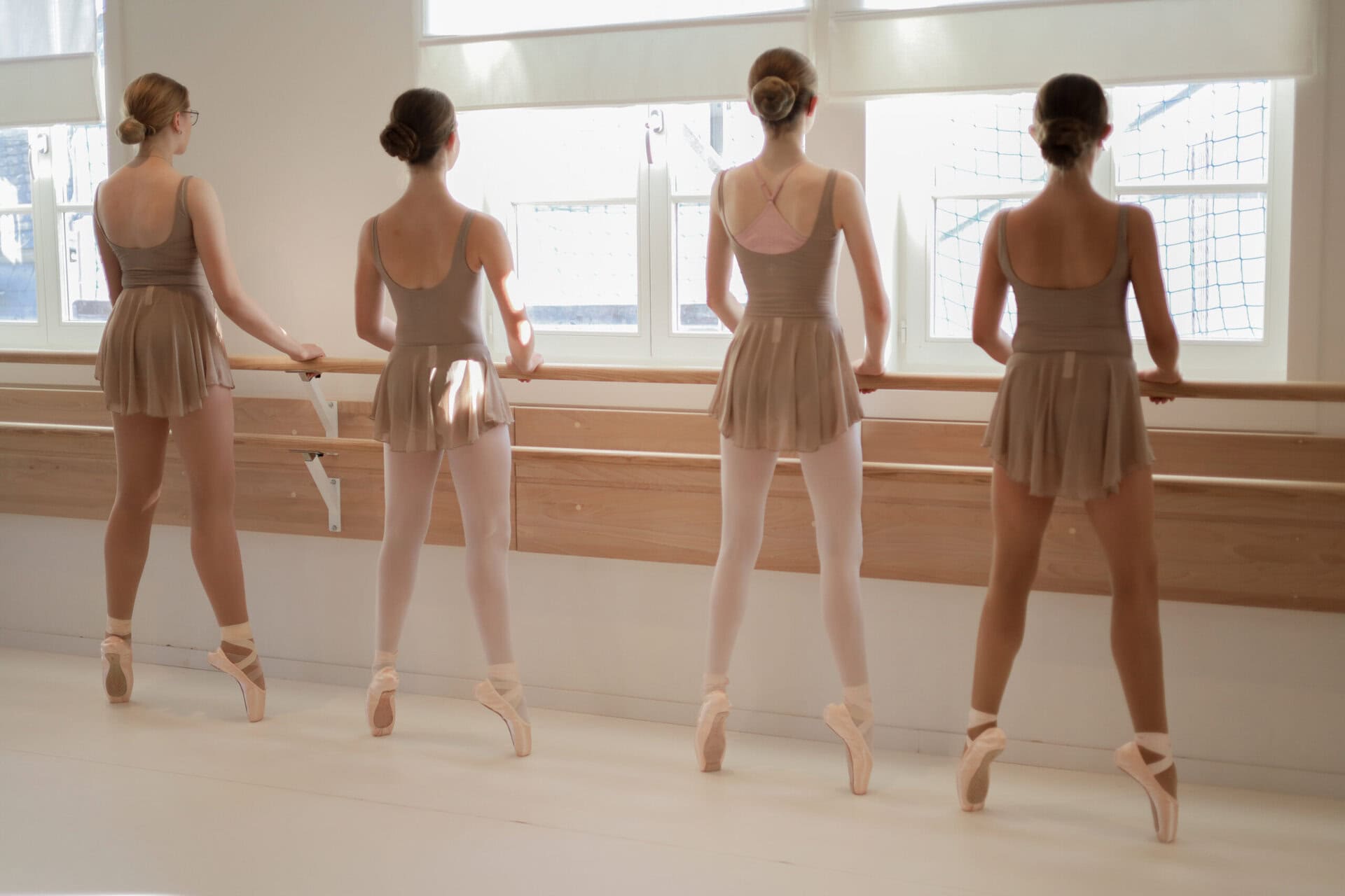Vier Ballettschülerinnen stehen an der Stange auf Spitze